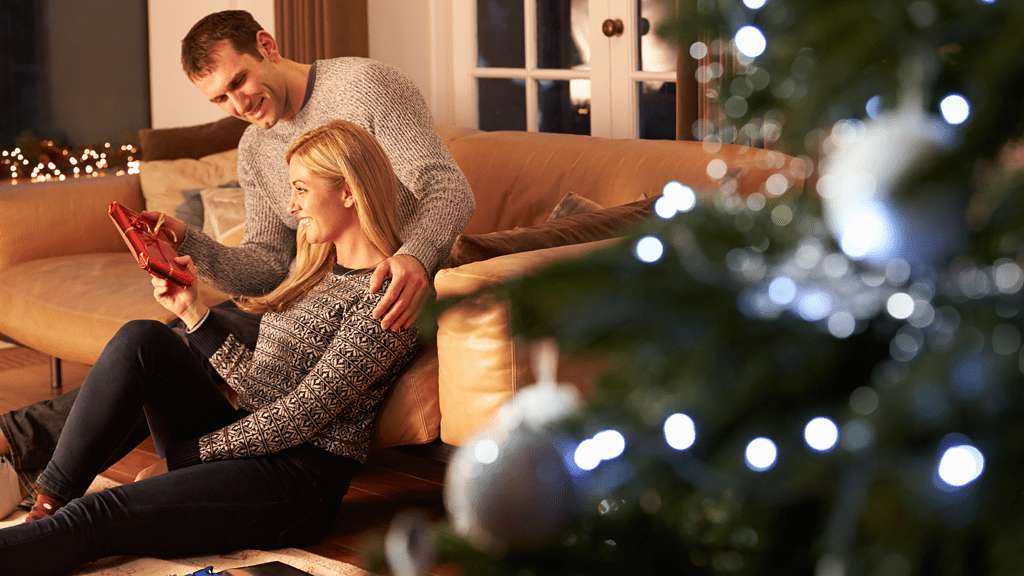 Couple exchanging gifts on couch with Christmas tree in the background
